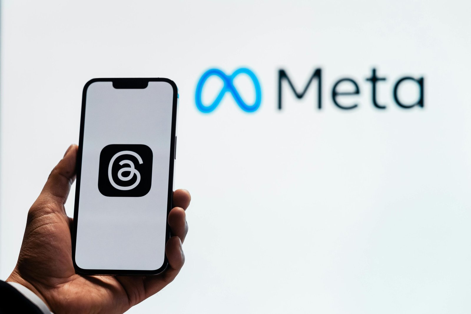 A hand holding a smartphone showing the Threads app with Meta logo in the background.